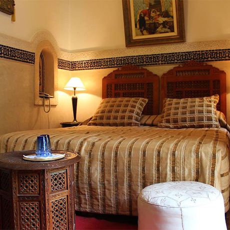 Blick auf ein Bett, zwei Hocker und einen Tisch im Schlafbereich des Standardzimmers Rubis