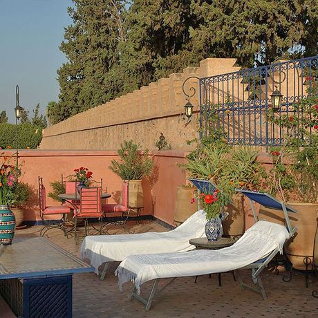 Blick auf zwei Liegen und einen Tisch mit Stuehlen auf der Dachterrasse des Riad Dar Al Kounouz