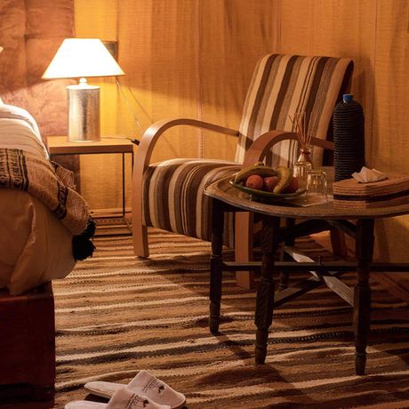 Blick auf ein Bett und einen Tisch mit Stuhl im Schlafbereich eines Luxuszeltes