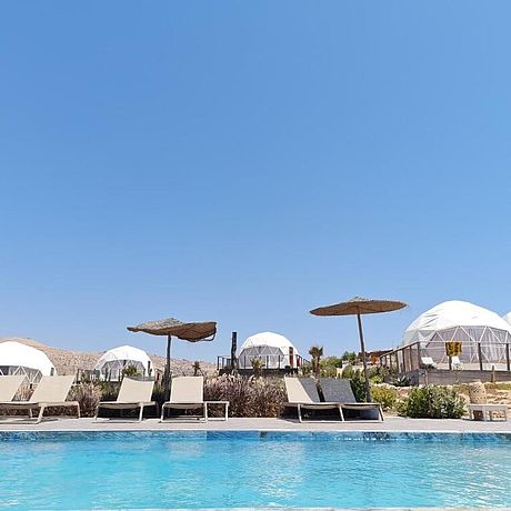 Blick auf Pool mit Sonnenliegen und Zelten